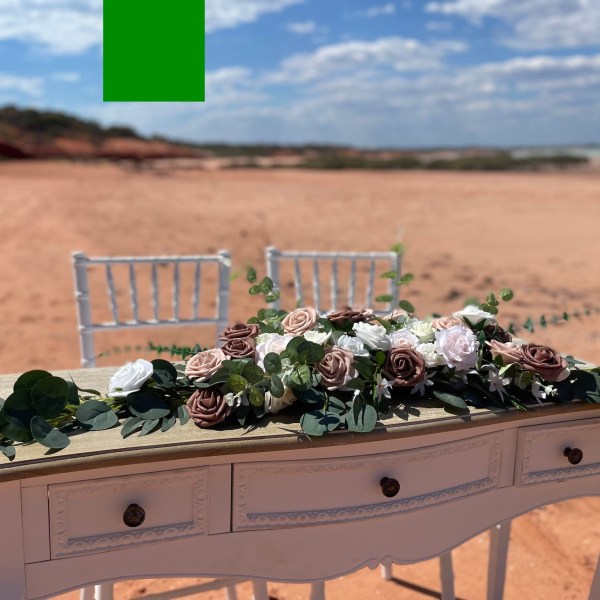 Floral arrangement on a white table on a sandy beach with two chairs.