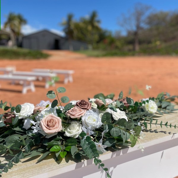 Floral arrangement with white and pink roses on a wooden surface, outdoor setting with benches in background.