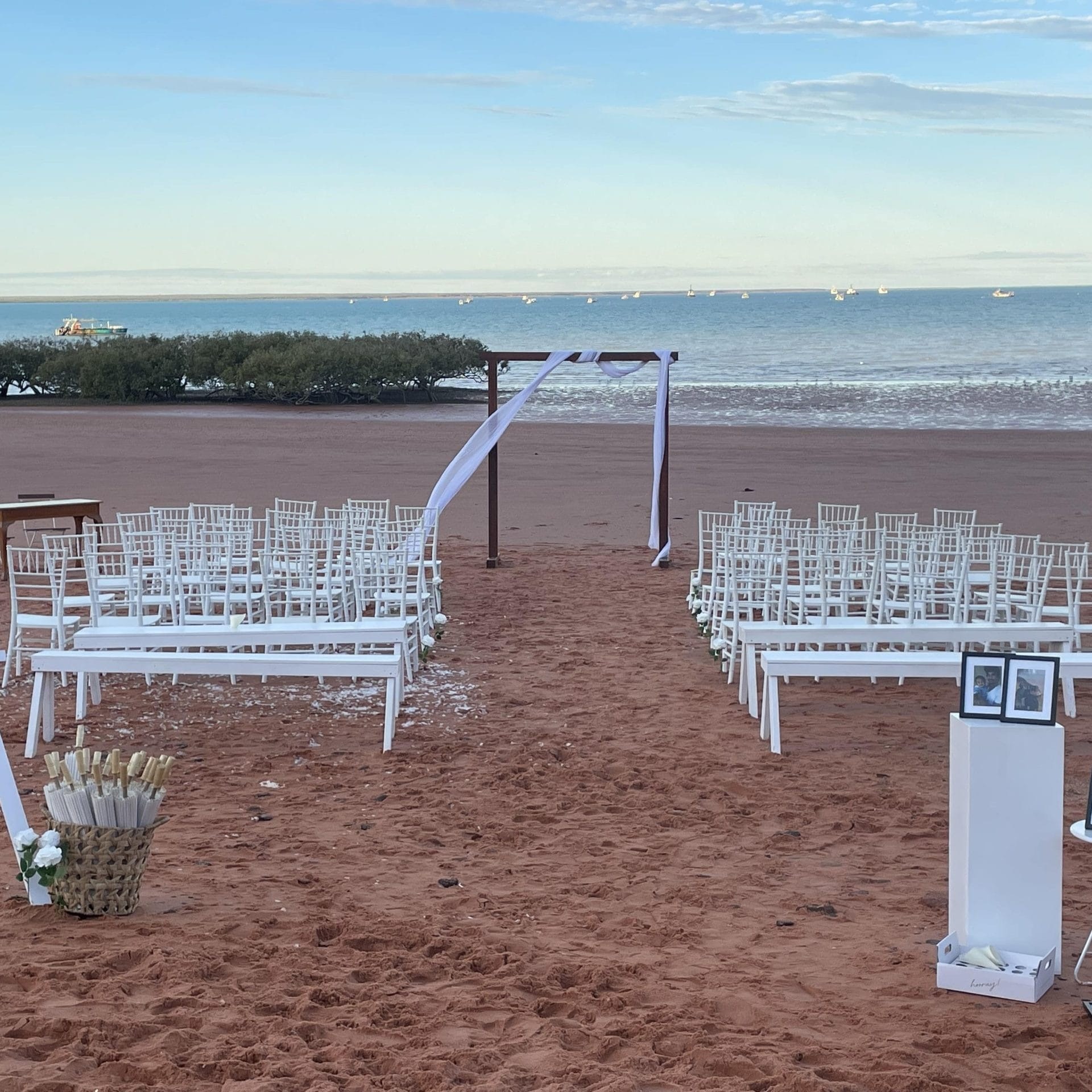 Beach wedding setup with chairs, arch, and a welcome sign on the sand.