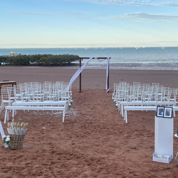 Beach wedding setup with chairs, arch, and a welcome sign on the sand.