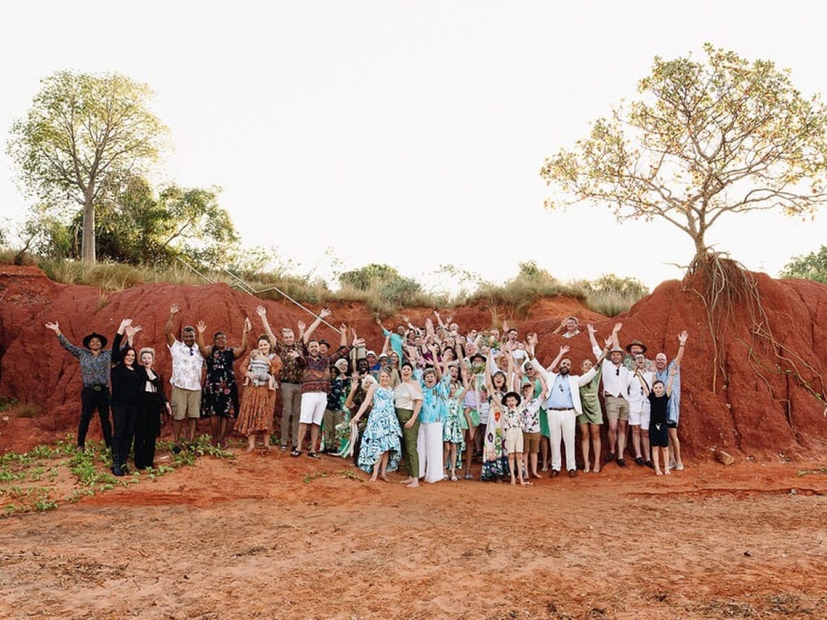 Large group of people cheering on red dirt with trees in the background.