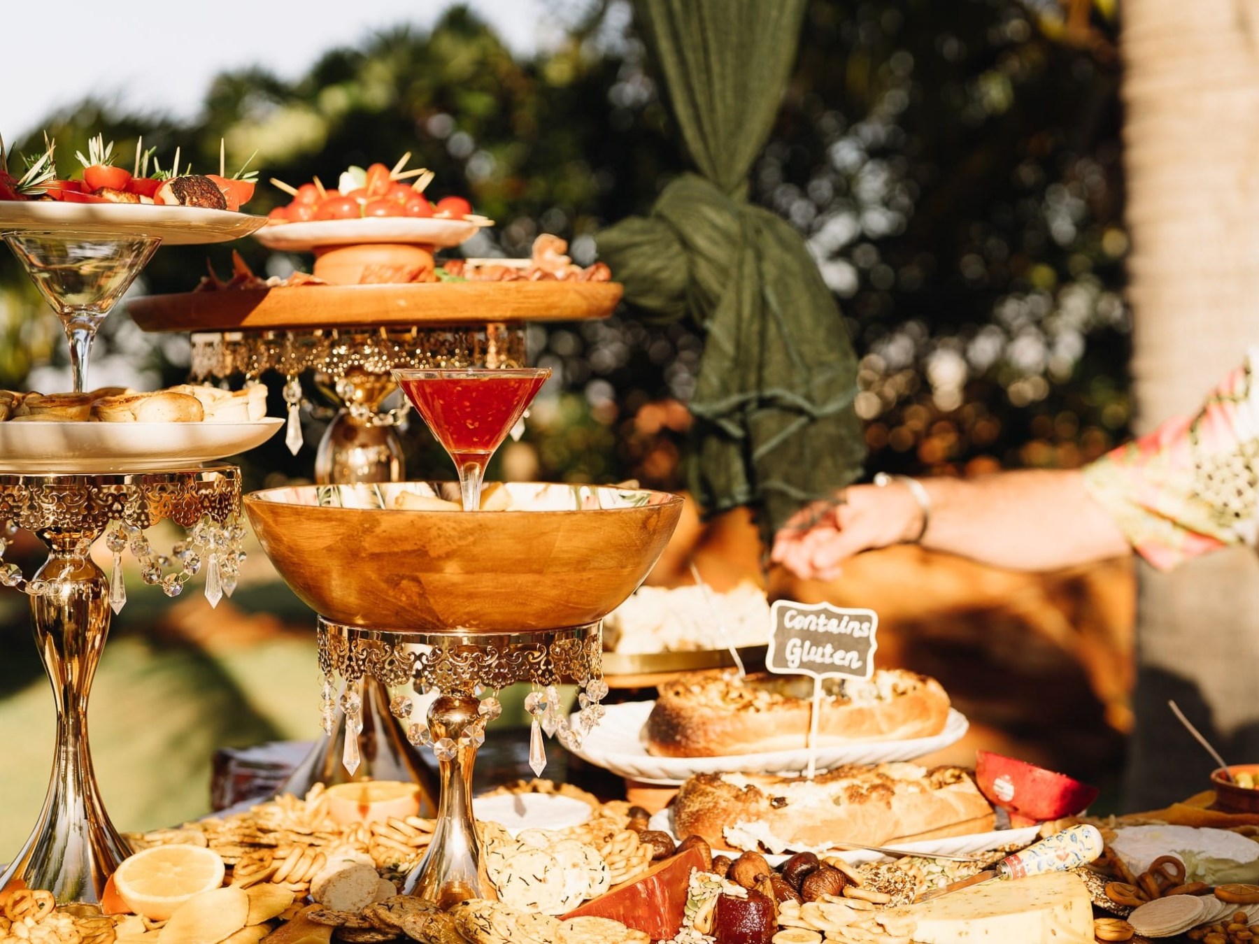 Outdoor buffet with platters of appetizers, drinks, and a gluten warning sign on gluten-containing food.