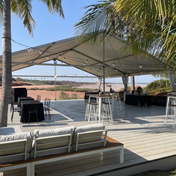 Outdoor event space with canopy, tables, stools, and palm trees overlooking a scenic landscape.