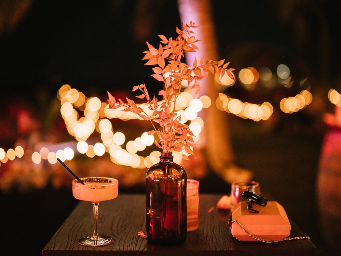 Table with drink and vase, fairy lights blurred in background at night.
