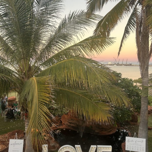 Palm trees and large lit 'LOVE' sign at outdoor event near water.