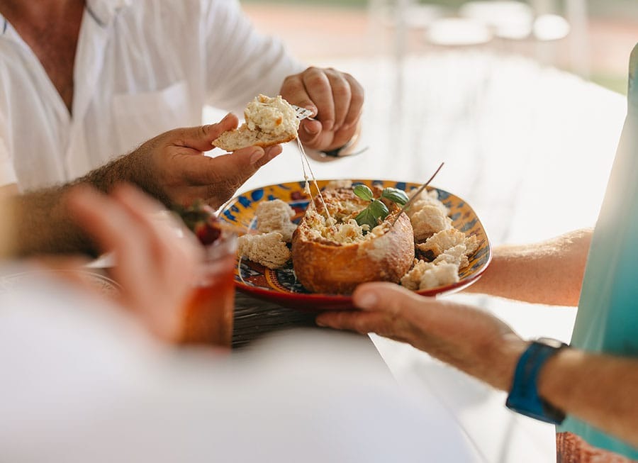 People sharing a bread bowl with dip on a colorful plate.