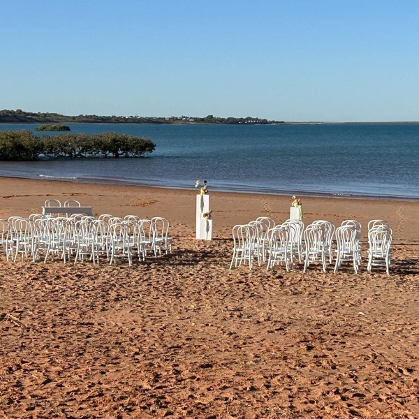 Rows of white chairs set up on a sandy beach, facing the ocean, with two small podiums.