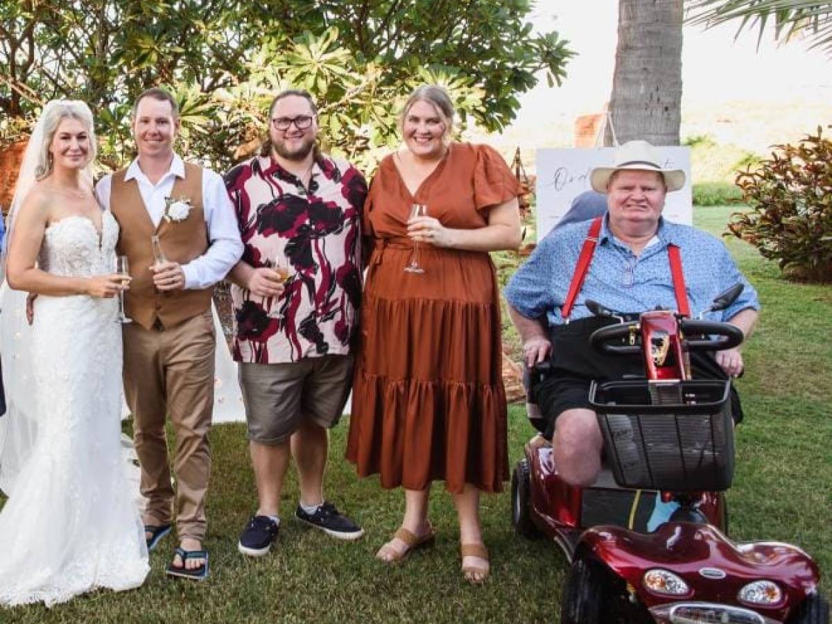Group of five people at an outdoor event, including a couple in wedding attire.